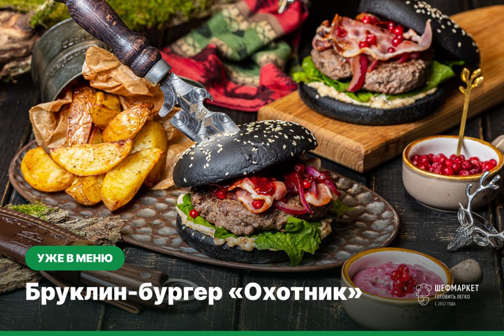 Бруклин-бургер «Охотник» с говяжьим бифштексом, беконом, кремом блю чиз и брусникой в чёрной булочке, рядом картофель «Айдахо»